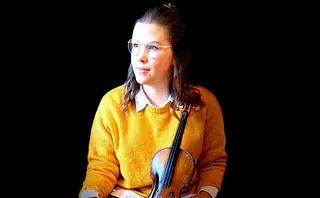 Junge Frau mit Brille hält Geige vor schwarzem Hintergrund.
