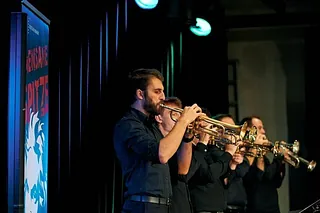 Vier Trompeter spielen Jazz auf einer dunklen Bühne.