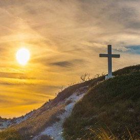 Einsames Kreuz auf grasbewachsenem Hügel unter lebhaftem Sonnenuntergangshimmel.