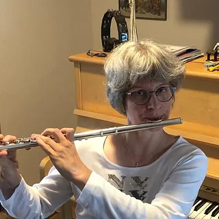  Frau mit Brille spielt die silberne Flöte im Innenraum.