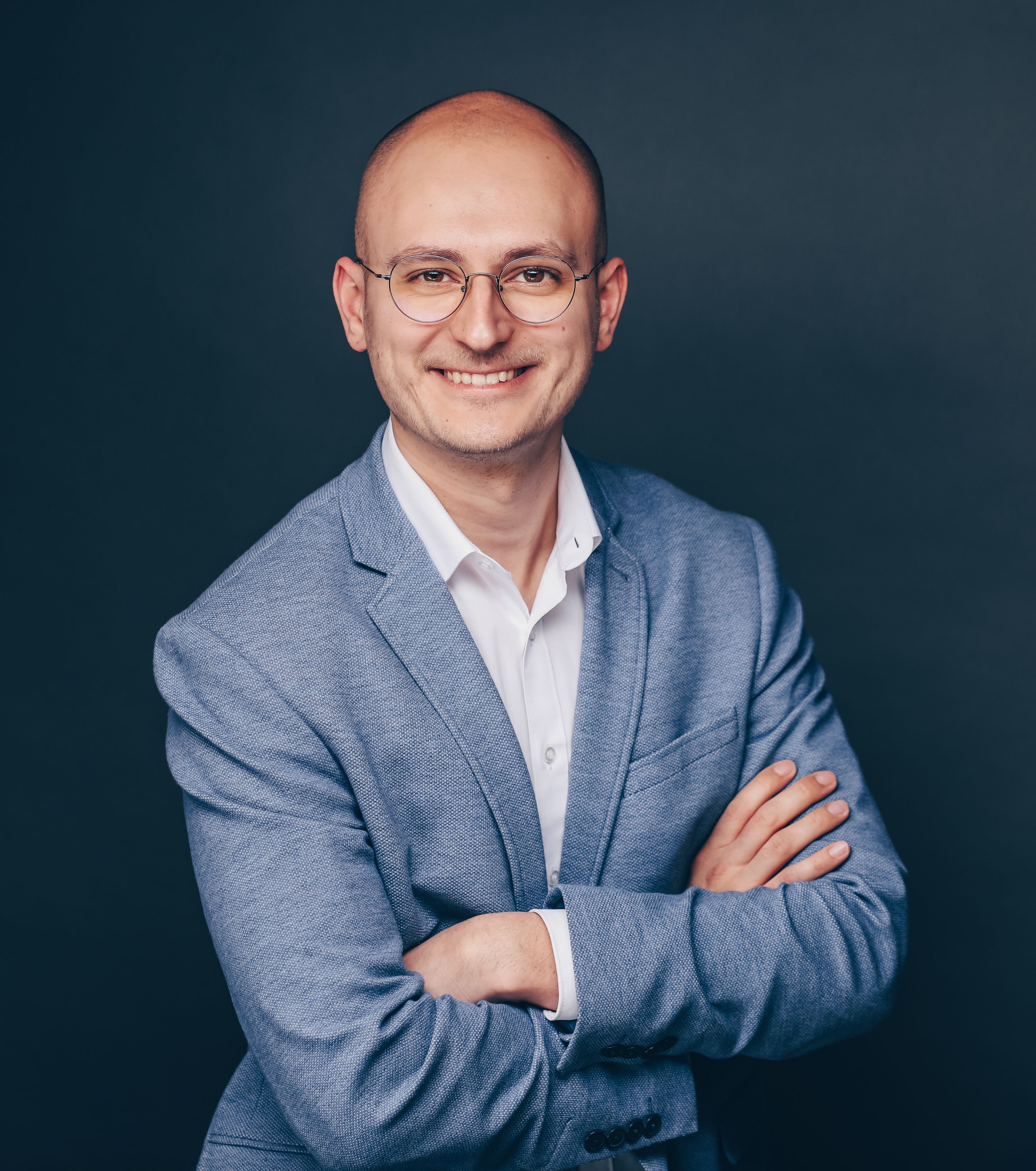 Lächelnder, kahler Mann mit Brille im blauen Blazer.