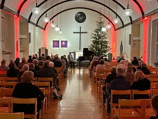 Publikum in Kirchenbänken blickt auf Redner und Weihnachtsbaum.