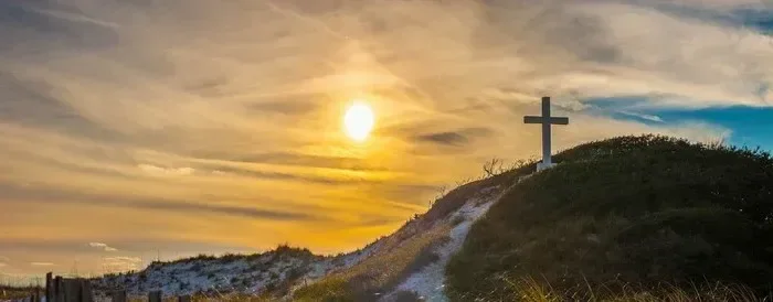 Gipfelkreuz steht vor einem dramatischen, farbenprächtigen Sonnenuntergang.