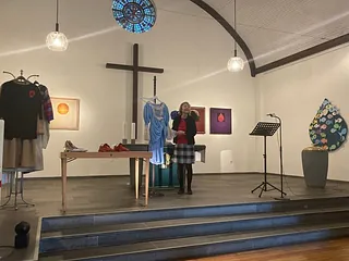 Frau spricht in Kirche mit Kunst- und Kleiderausstellung.