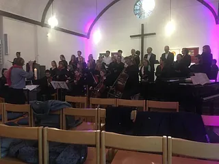 Chor und Orchester treten in einer hell erleuchteten Kirche auf.